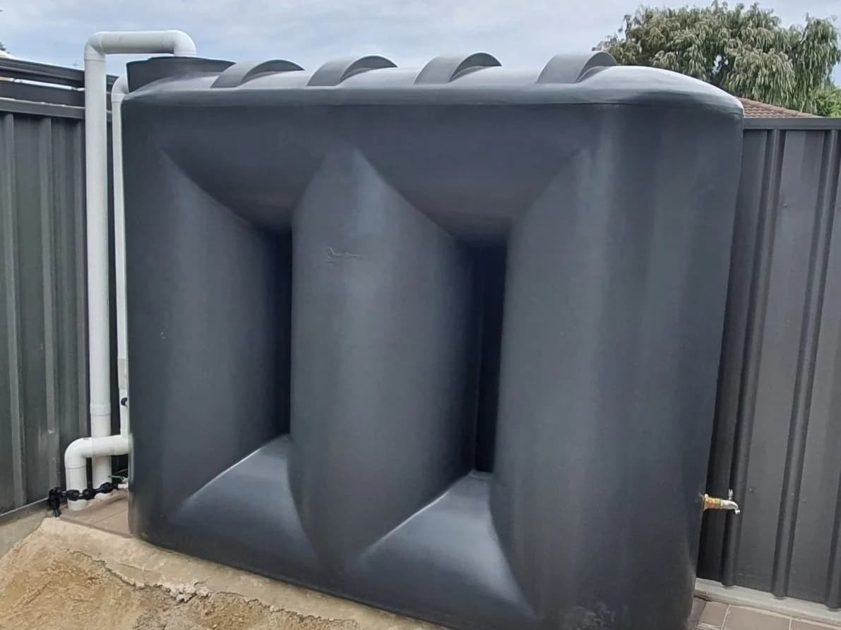 Slim-line rainwater tank with completed PVC plumbing and brass tap connection against a fence